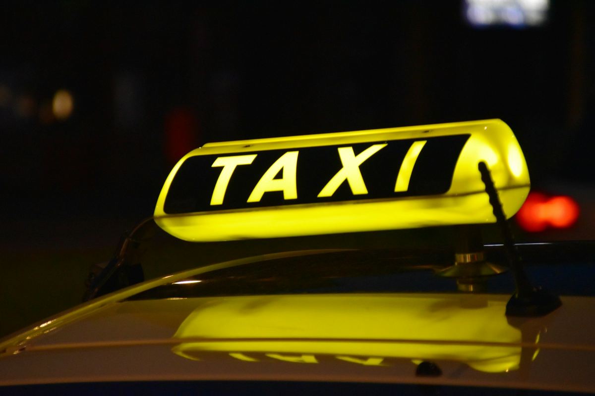 A yellow taxi roof sign glowing at night on top of a cab